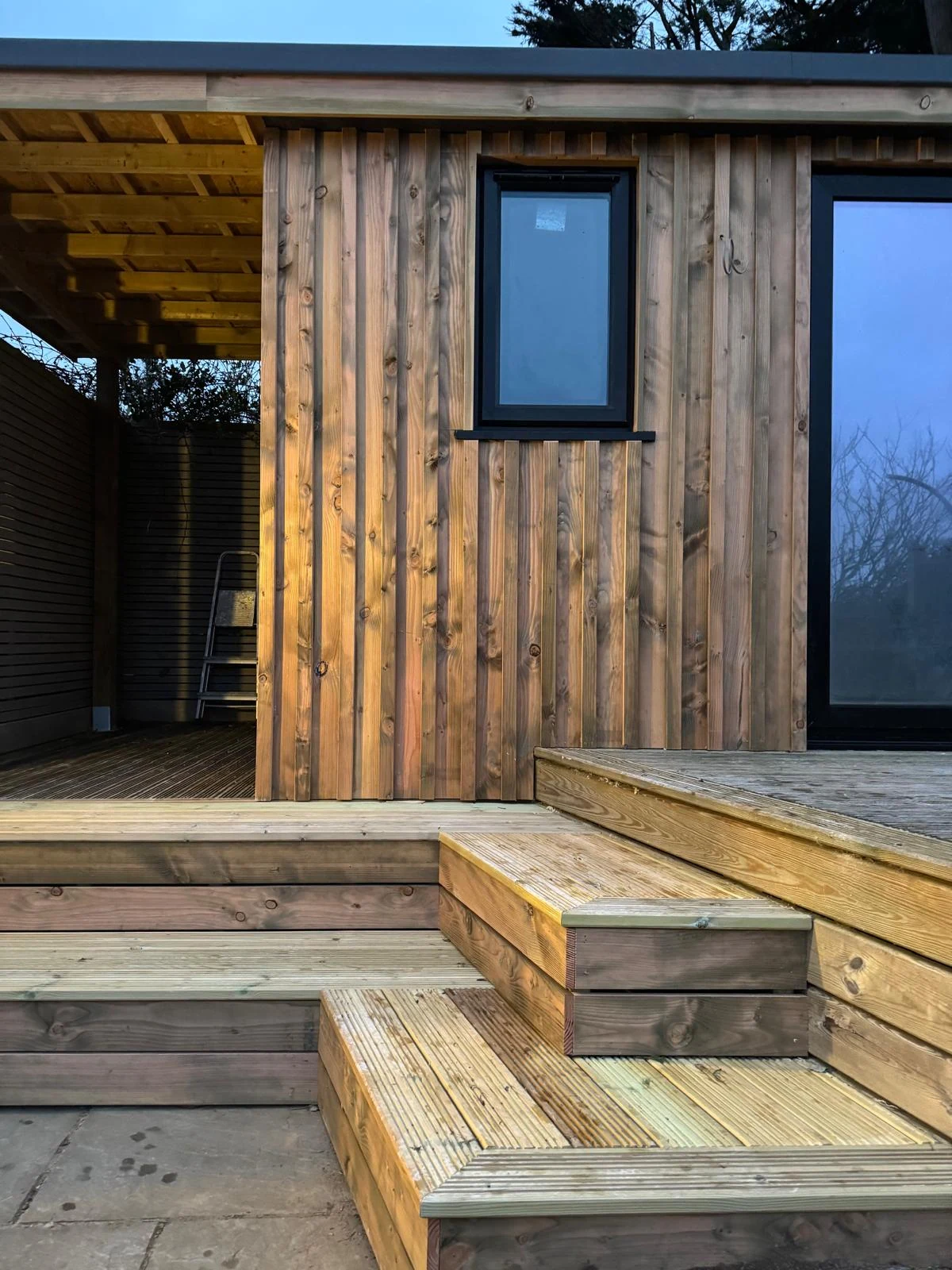 Timber-clad garden office corner with sliding doors and deck steps