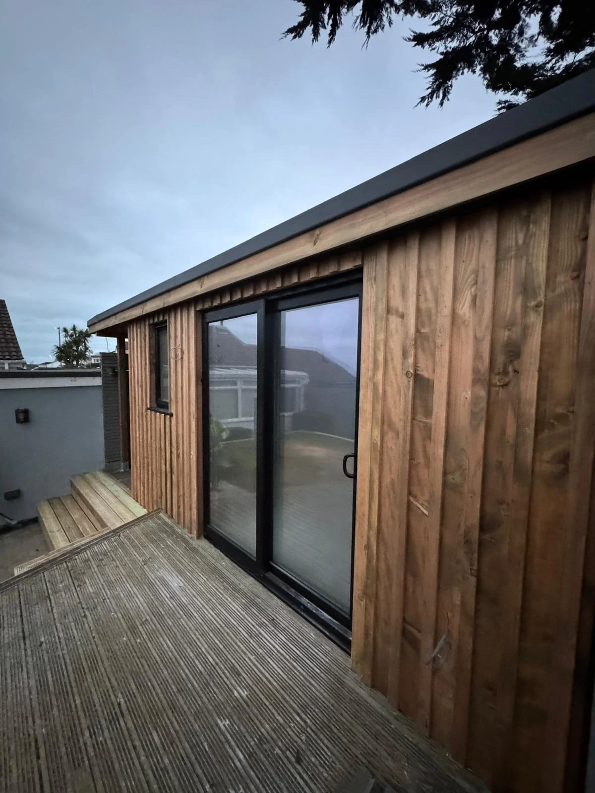 Timber-clad garden office with sliding glass doors and decking