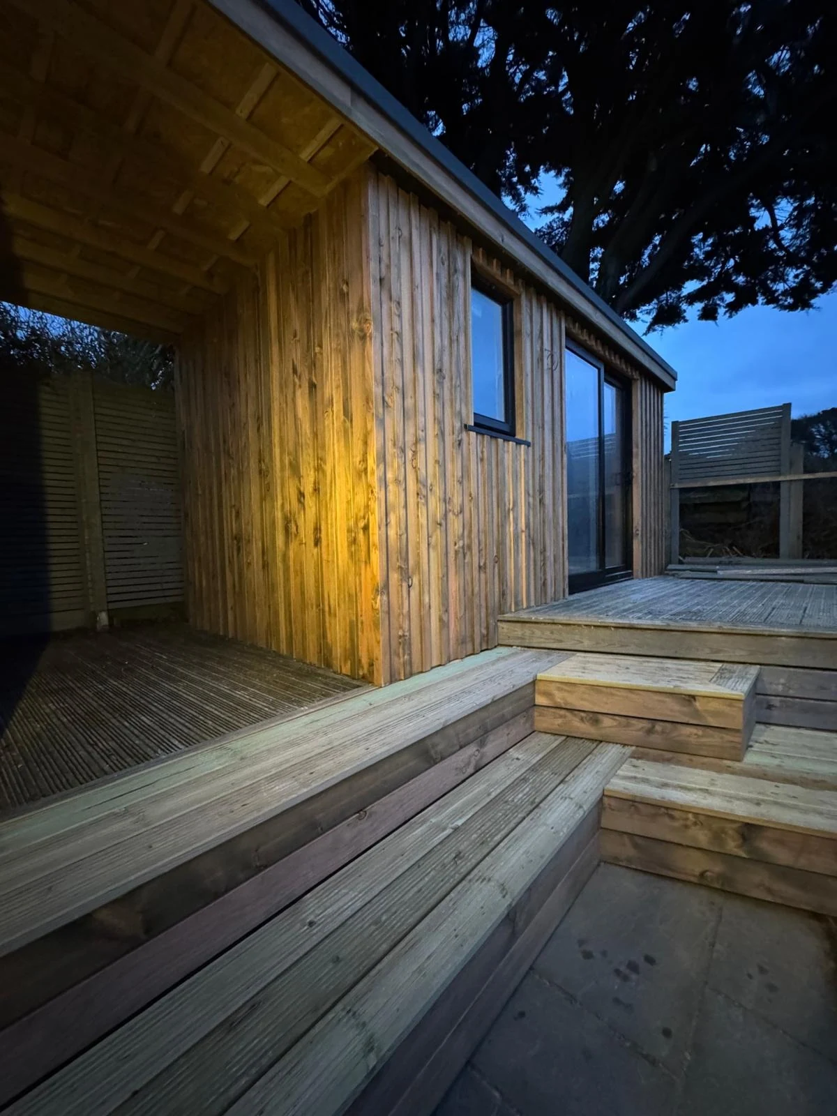 Bespoke garden office with warm-lit cladding and raised decking