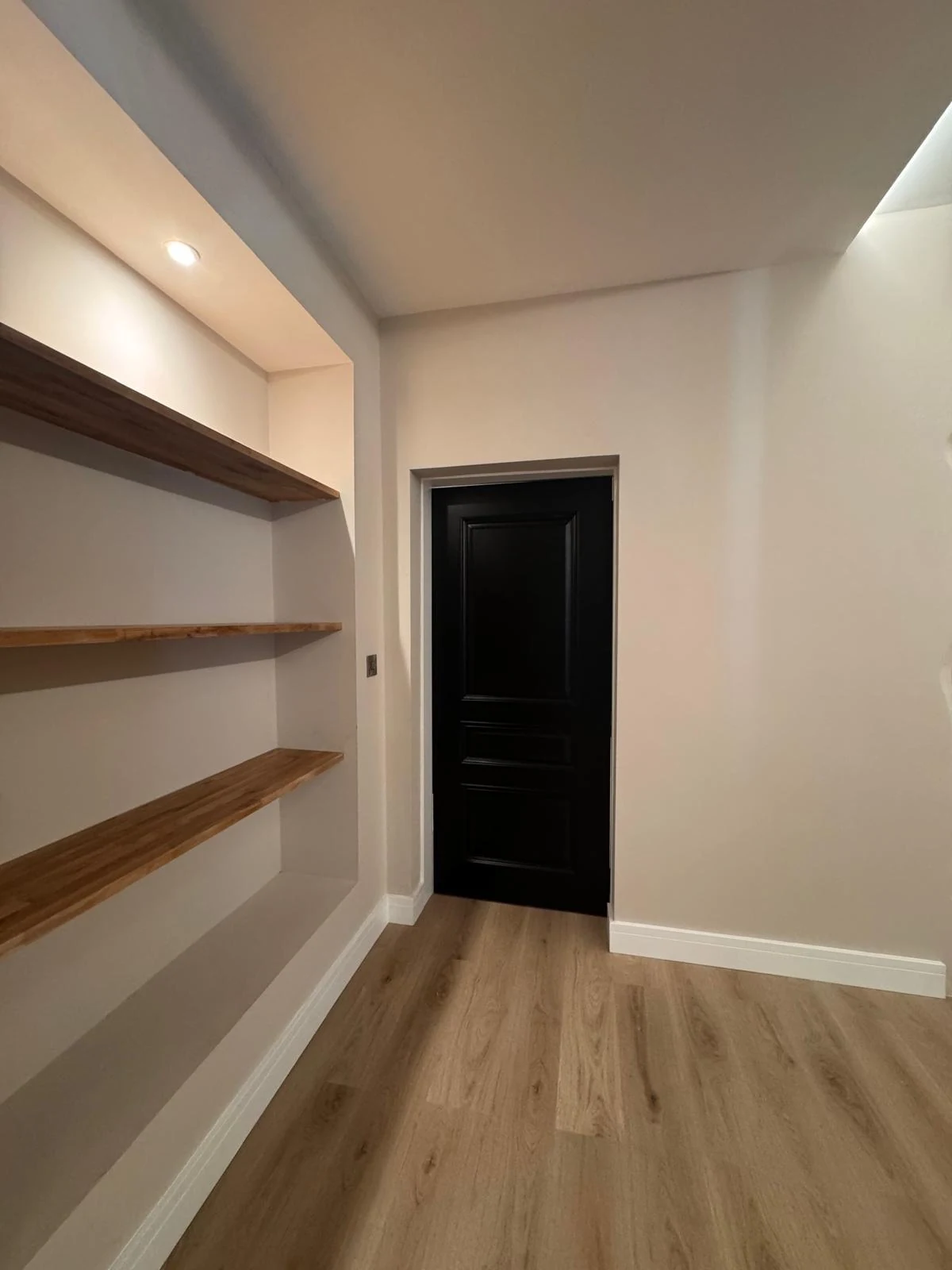 Floating oak shelves in an alcove beside a black internal door