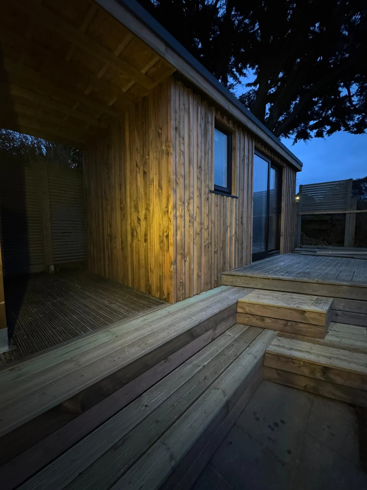 Timber-clad garden office and stepped decking under a mature tree