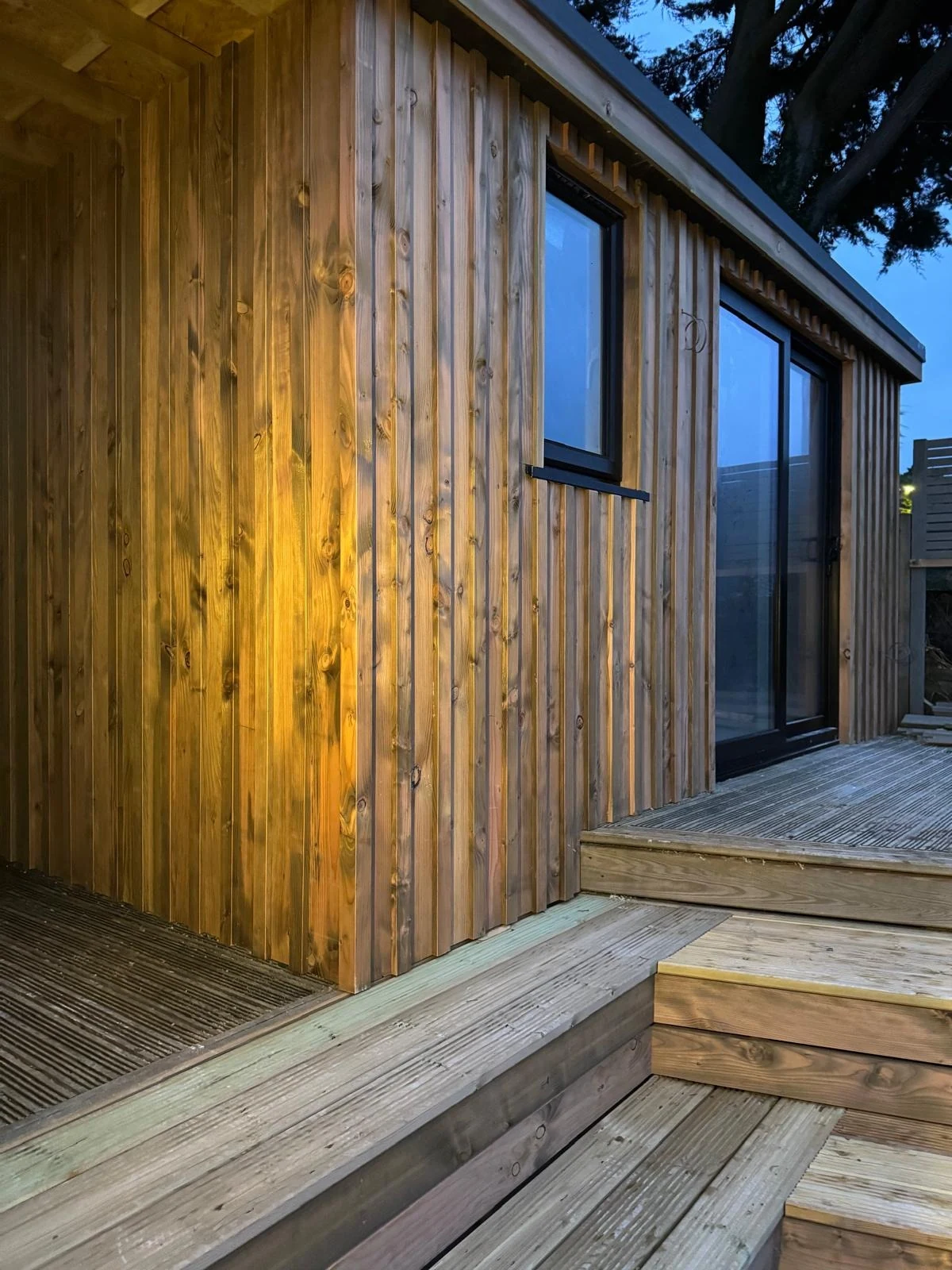 Warm-lit timber-clad garden office wall and deck steps